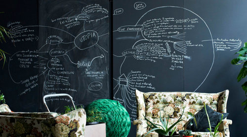 An industrial-styled loft. The centerpiece of the photo is a blackboard filling the entire rear wall. On it is a mind map for a proposed utopia. Selected fragments of the map include "Turn thoughts and intentions into actions", "Laughing", and "Mass production is good!". There are dozens of these and they're all like this.